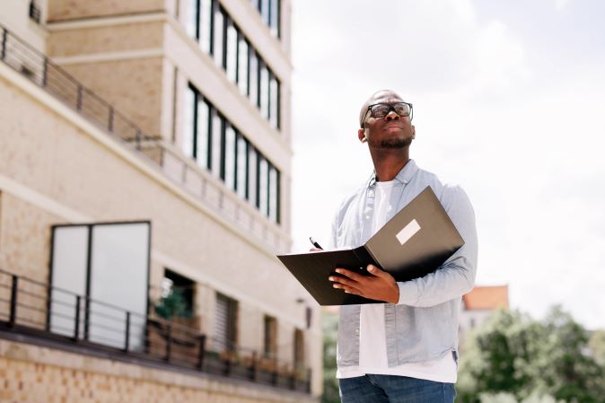 Man with glasses and open file standing outside building