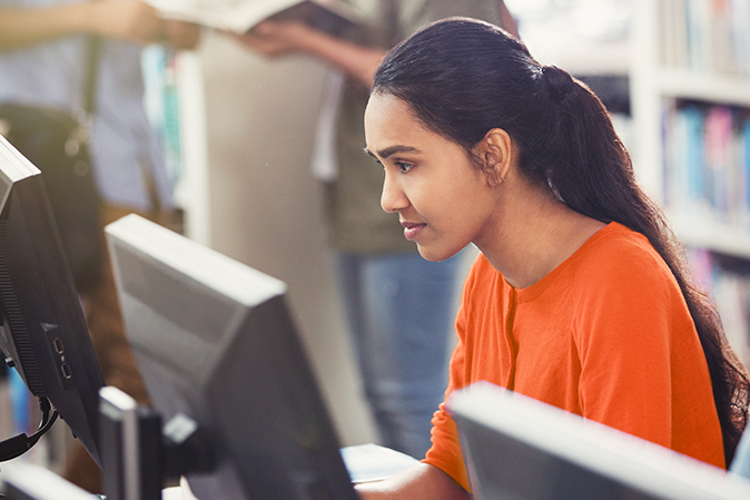 Focused female college student researching using computer in library