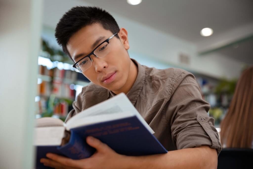 Male student reading a book in a library
