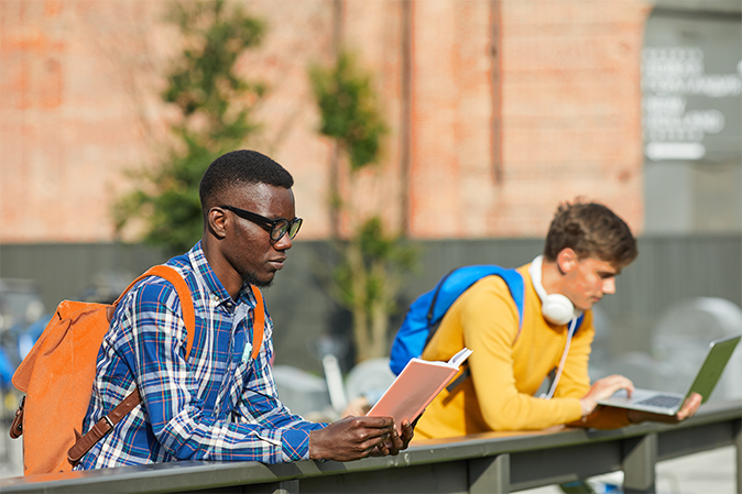 Portrait of African-American student reading book outdoors in sunlight, copy space