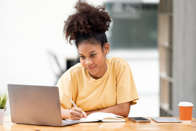 Female student taking notes in journal while looking at laptop