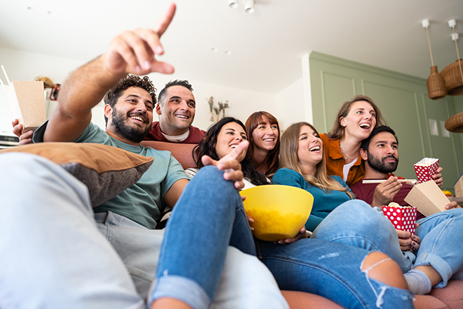 Group of college students sitting on a couch eating snacks while watching a movie