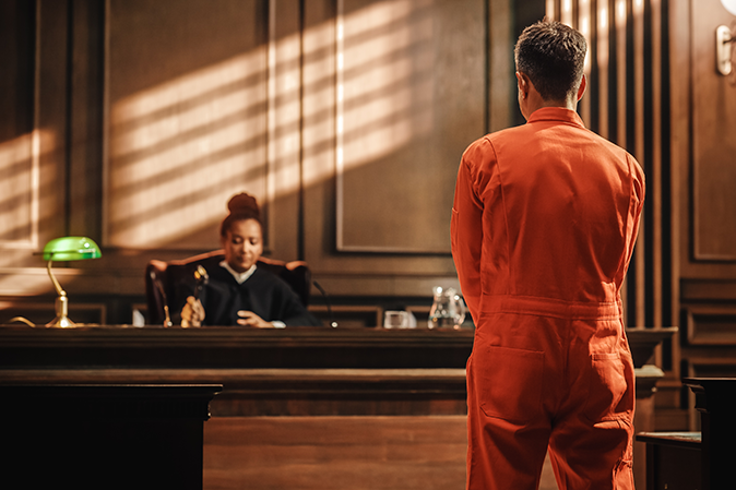 The accused in a prison outfit standing before a judge in a courtroom