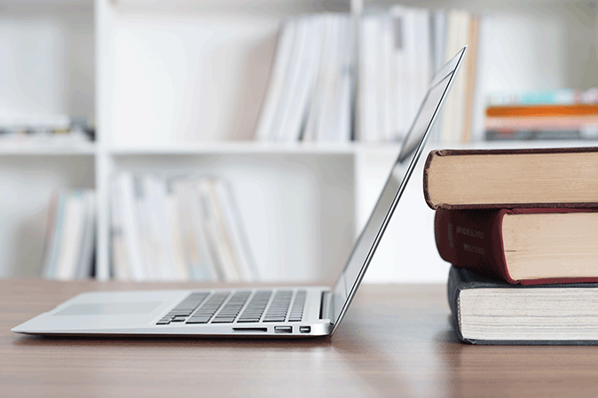 Laptop on a desk next to a stack of books