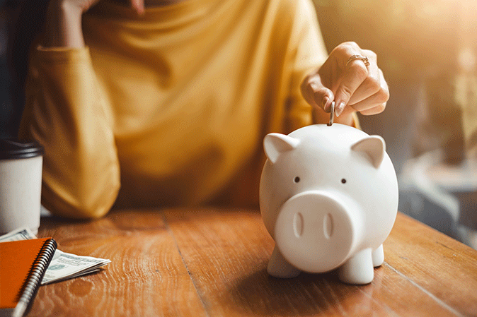 Woman dropping a coin into a piggy bank sitting on the table