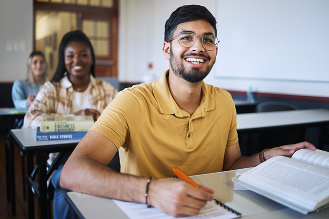 Young man smiling in class with an open book and taking notes