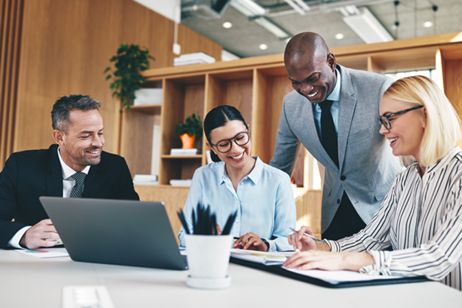 Four office employees gathered around a laptop and smiling
