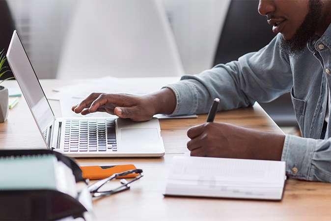 African American male student taking notes from laptop
