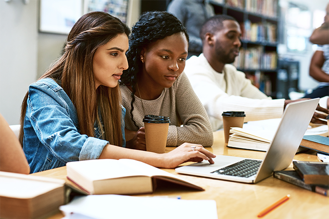 Two young women studying together on a laptop in a library