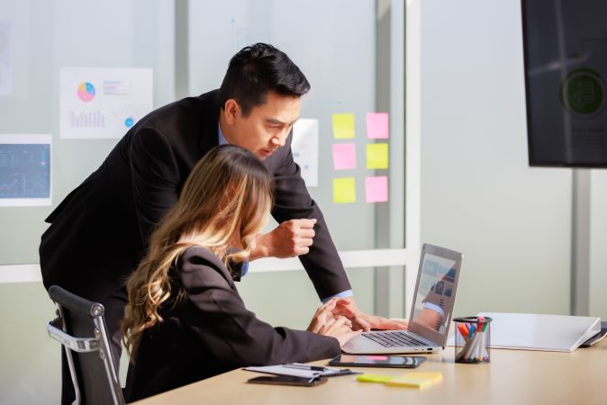 Man and woman collaborating on a laptop in an office meeting.