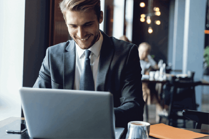 Young man in a suit smiling while working on a laptop
