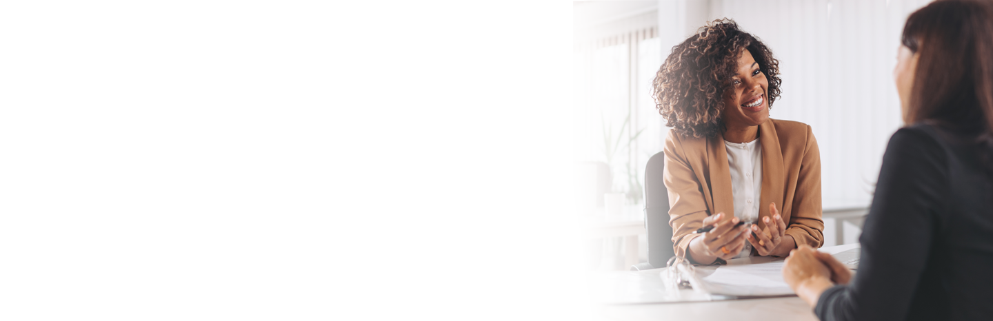 Young professional woman having a discussion at a desk with another young professional woman