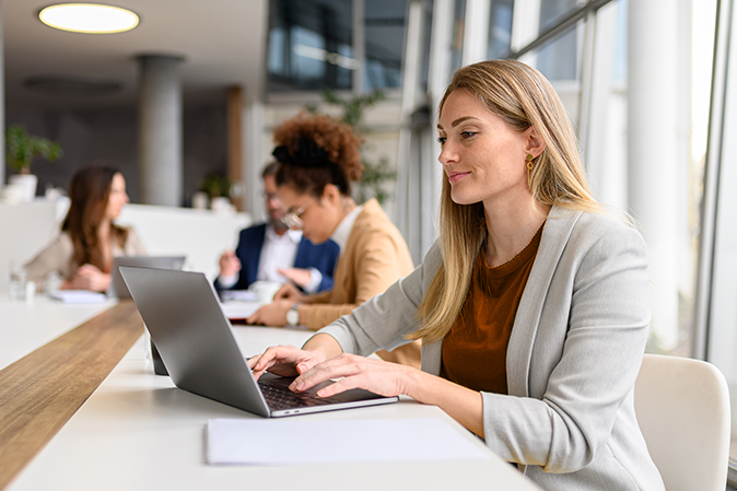 Confident female professional analyzing report over laptop while working with colleagues in the meeting room