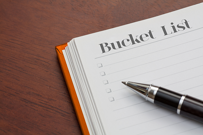 A pen sitting on a notebook that says Bucket List with rows of checkboxes