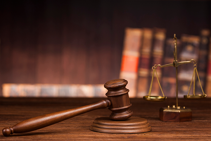 A judge's gavel next to scales of justice with law books in the background