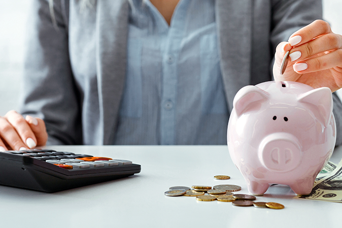 Woman with a calculator dropping coins into a piggy bank