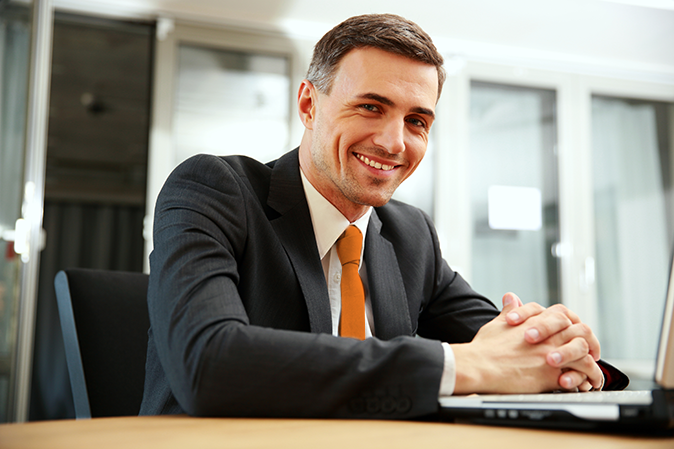 Lawyer smiling at his desk with hands on his laptop