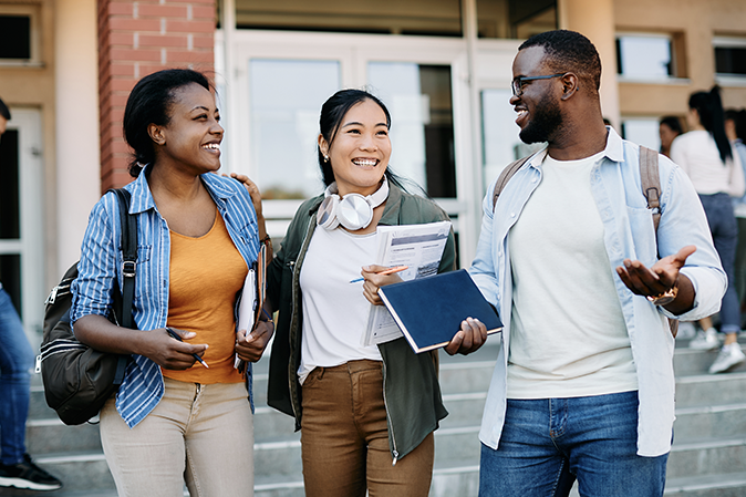 Three students smiling and talking while walking outside a campus building