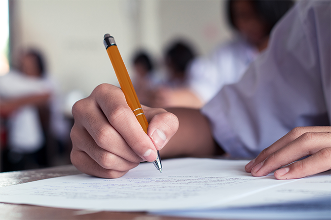 Young college student holding an orange pen taking a test in class