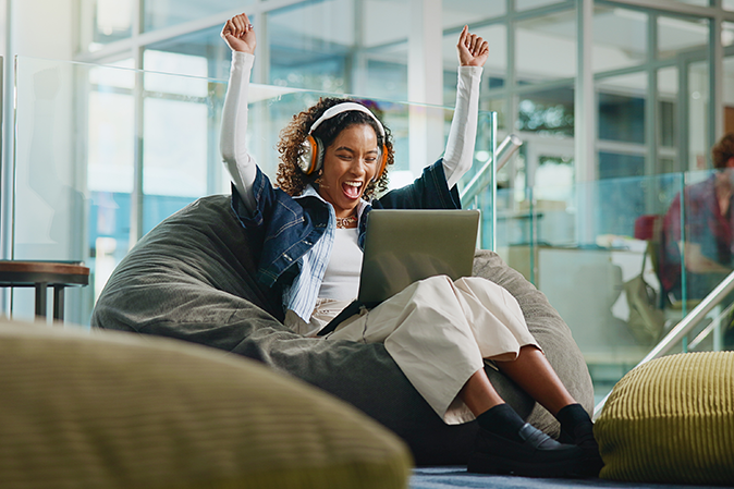 Young woman wearing headphones with a laptop in a study hall showing excitement