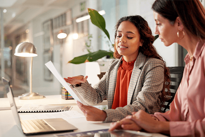 Young woman working with a senior member on paperwork in front of a laptop